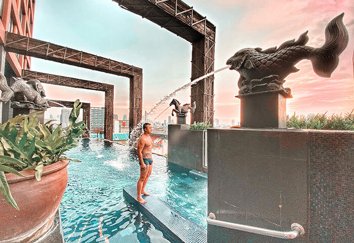 Siam @ Siam Design Hotel Bangkok pool view. Gay-friendly hotel with man in swimwear. Fish and horse statues with water feature.
