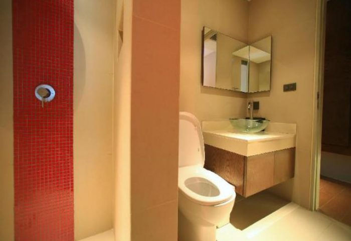 Bathroom at Gay-Friendly Silom One Hotel. Features a red-tiled shower, toilet, and vanity with a glass bowl sink and mirrored cabinet.