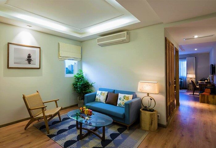 Silverland Yen Hotel's living room. Gay-friendly hotel with a blue sofa, wooden chair, glass table, and modern decor. A comfortable space for travelers.