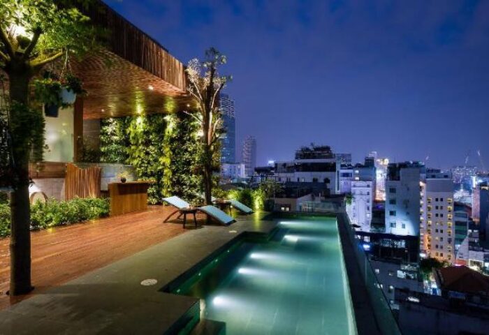 Rooftop pool at night in Gay-Friendly Silverland Yen Hotel. Deck chairs, lush greenery, and city views. A luxurious gay travel destination.