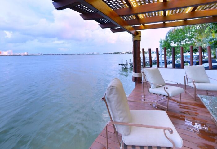 Sina Suites gay-friendly hotel patio. Waterfront view with chairs on a wooden deck under a pergola. Relaxing travel for gay men.