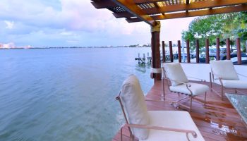 Sina Suites gay-friendly hotel patio. Waterfront view with chairs on a wooden deck under a pergola. Relaxing travel for gay men.