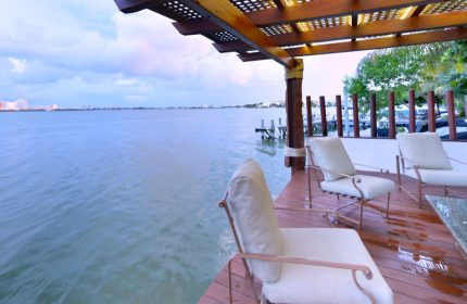 Sina Suites gay-friendly hotel patio. Waterfront view with chairs on a wooden deck under a pergola. Relaxing travel for gay men.