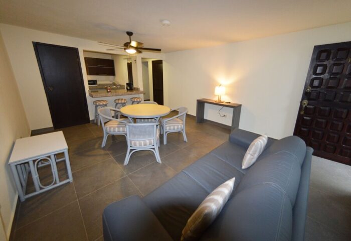 Sina Suites gay-friendly hotel room. Living area with sofa, table, and chairs. Kitchen in background. Comfortable lodging for gay travelers.