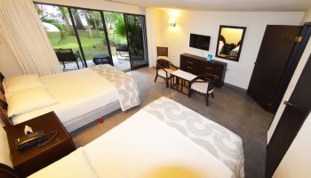 Sina Suites gay-friendly hotel room. Two beds, patio access, TV, and seating area. A comfortable space for gay travelers to relax.
