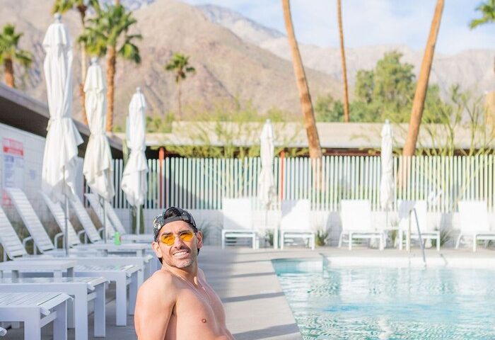 Gay-friendly Skylark Hotel pool view. Man in swim trunks relaxing by the pool with mountains and palm trees in the background. Gay travel advice.