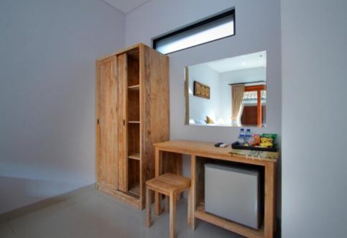 Sleepwell Seminyak gay-friendly hotel room. Wooden wardrobe, desk with mini fridge, and stool. Mirror reflecting the bed and window. Minimalist decor.