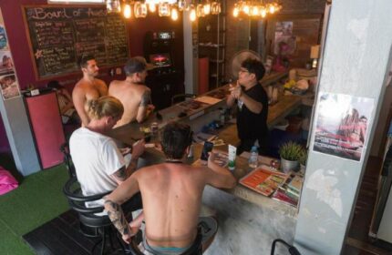 Gay-friendly Beach Hostel slumber party. Men at the bar talking to the bartender. Gay travel advice. Relaxed atmosphere.