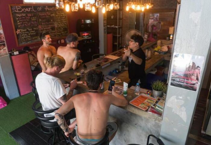 Gay-friendly Beach Hostel slumber party. Men at the bar talking to the bartender. Gay travel advice. Relaxed atmosphere.