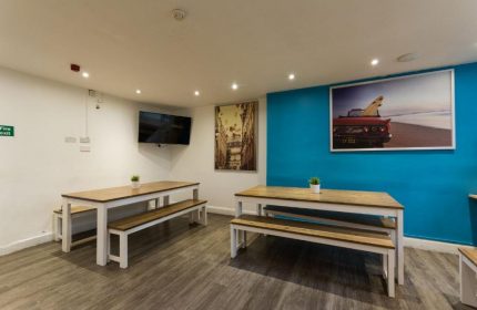Smart Hyde Park Inn Hostel dining area. Gay-friendly hotel with tables, benches, and artwork. Ideal for gay men's travel in London.