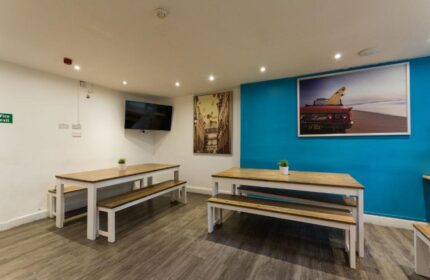 Smart Hyde Park Inn Hostel dining area. Gay-friendly hotel with tables, benches, and artwork. Ideal for gay men's travel in London.