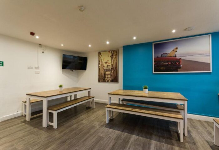 Smart Hyde Park Inn Hostel dining area. Gay-friendly hotel with tables, benches, and artwork. Ideal for gay men's travel in London.