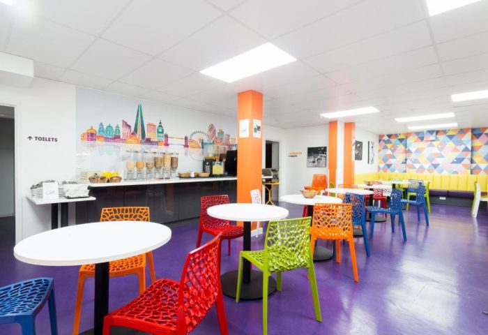 So Hostel's dining area, a gay-friendly hotel. Colorful chairs and tables on a purple floor. London skyline mural. Breakfast buffet.