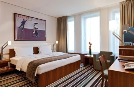 Dorint Kurfurstendamm Hotel room. Gay-friendly hotel, pet-friendly. Modern design, large bed, desk, chair, and artwork. Berlin hotel.