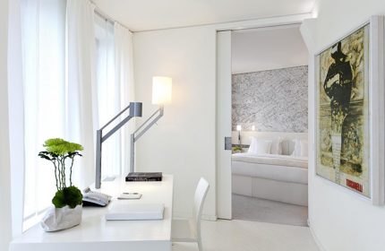 Dorint Kurfurstendamm Hotel's pet-friendly room. Modern design, white desk, stylish lamp, and a glimpse into the bedroom. Gay-friendly hotel.