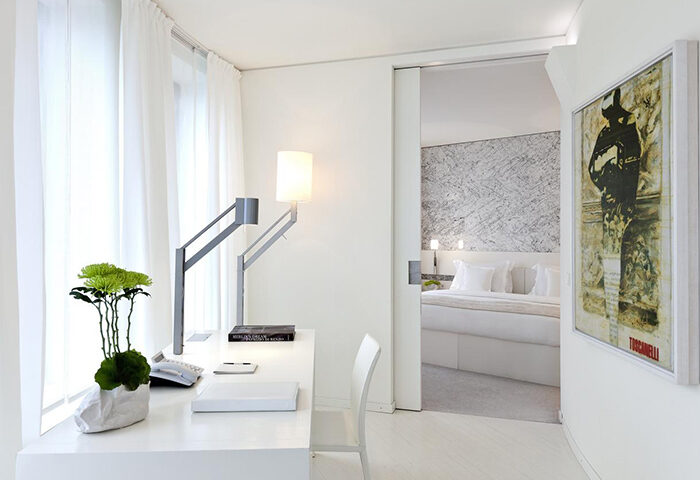 Dorint Kurfurstendamm Hotel's pet-friendly room. Modern design, white desk, stylish lamp, and a glimpse into the bedroom. Gay-friendly hotel.