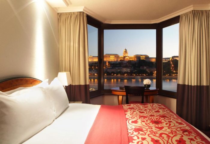 Sofitel Budapest Hotel room with Danube view. Gay-friendly, pet-friendly hotel. Room with bed, desk and river view of Budapest at dusk.
