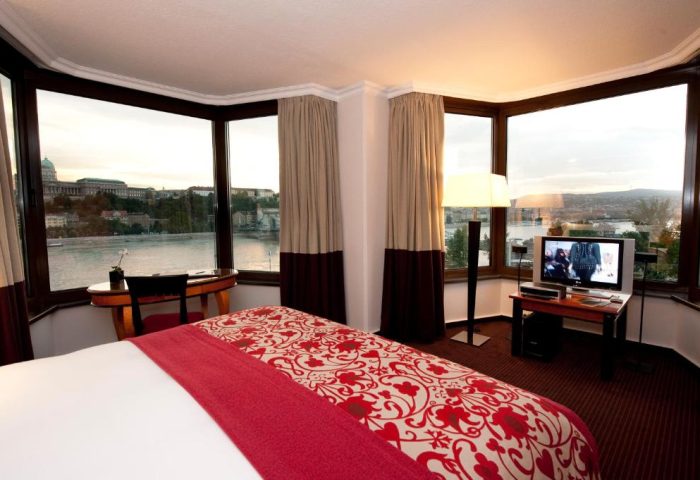 Sofitel Budapest Hotel room with river view. Gay-friendly, pet-friendly hotel. Room with a bed, TV, desk, and large windows overlooking the Danube.