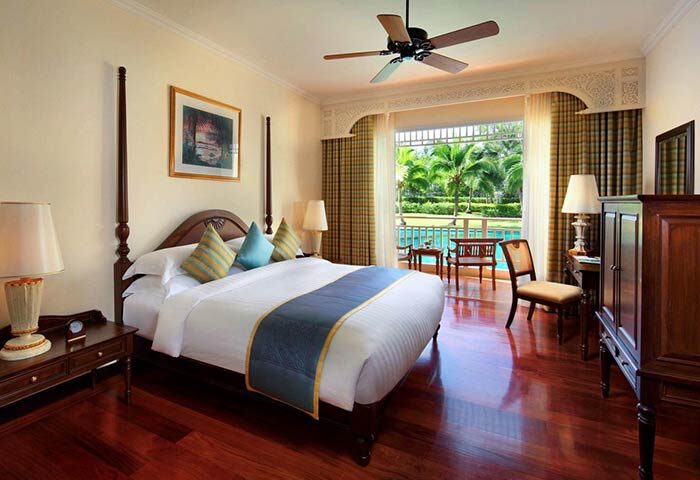 Sofitel Krabi Phokeethra Golf and Spa Resort room. Gay-friendly hotel with a bed, ceiling fan, and balcony overlooking the pool and palm trees.