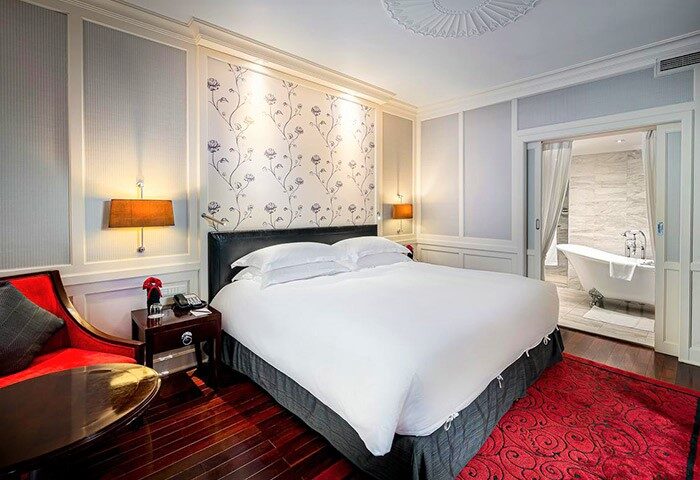 Sofitel Legend Metropole Hanoi Hotel room. Gay-friendly hotel with bedroom, bathroom, tub, red chair, and floral wallpaper. Luxury travel.