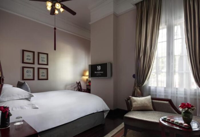 Gay-friendly Sofitel Legend Metropole Hanoi Hotel room. Luxury bedding, chaise lounge, and ceiling fan. Hanoi hotel for gay men travelers.