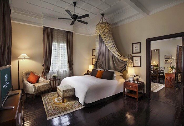 Bedroom at the gay-friendly Sofitel Legend Metropole Hanoi Hotel. A luxury room with a canopy bed, dark wood floors, and elegant furnishings.