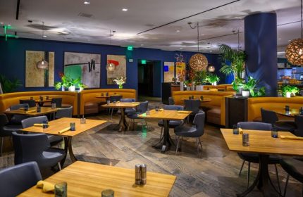 Sofitel Los Angeles at Beverly Hills Hotel gay-friendly restaurant. Booths, tables, and chairs in a stylish dining area. Modern decor, plants.