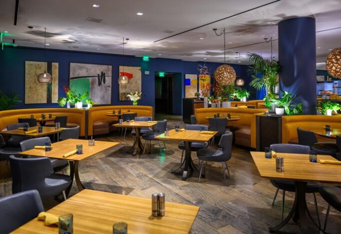 Sofitel Los Angeles at Beverly Hills Hotel gay-friendly restaurant. Booths, tables, and chairs in a stylish dining area. Modern decor, plants.