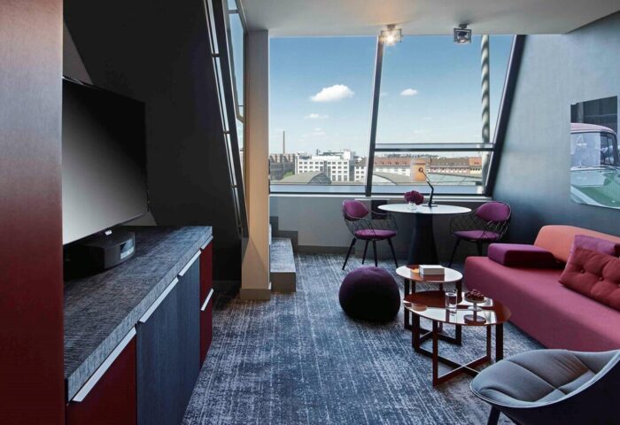 Sofitel Munich Bayerpost Hotel room. Gay-friendly hotel with modern design, city view, sofa, and table with chairs. Upscale travel experience.