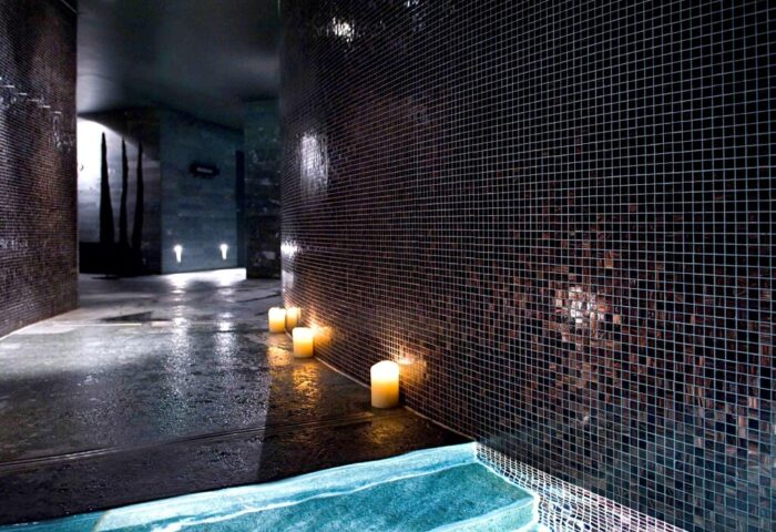 Sofitel Munich Bayerpost Hotel's spa area. Candles light the way in this gay-friendly hotel. Mosaic tiles line the walls near a pool.