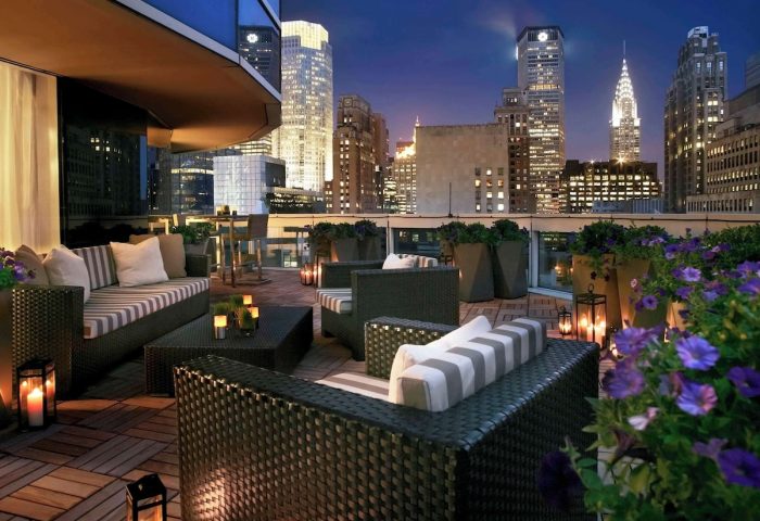 Sofitel New York gay-friendly hotel rooftop lounge at night. City skyline view, stylish seating, and flowers. Luxury travel for gay men.