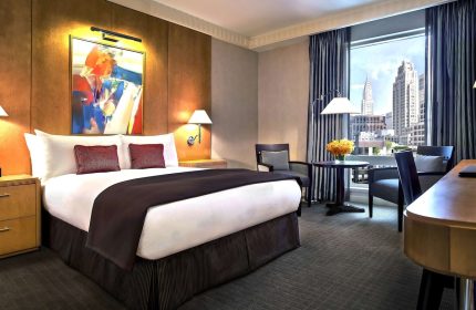 Sofitel New York hotel room. Gay-friendly hotel with a bed, chairs, desk, and a view of the New York City skyline, including the Chrysler Building.