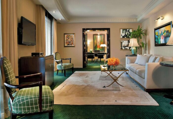 Sofitel New York suite living room. Gay-friendly hotel with sofa, chairs, TV, and desk visible through doorway. Upscale travel for gay men.