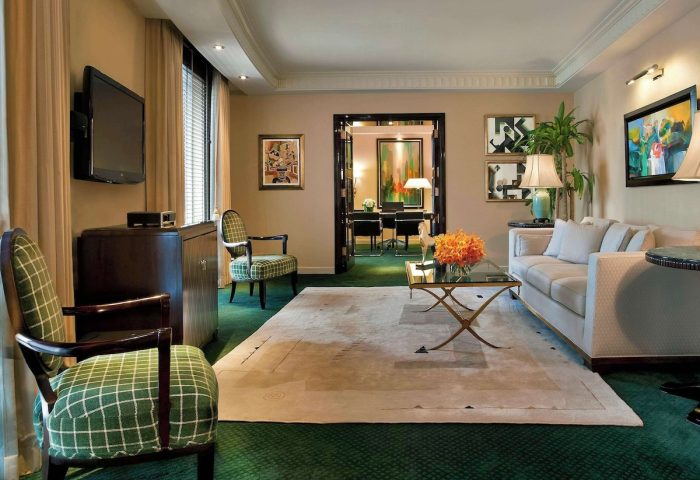 Sofitel New York suite living room. Gay-friendly hotel with sofa, chairs, TV, and desk visible through doorway. Upscale travel for gay men.