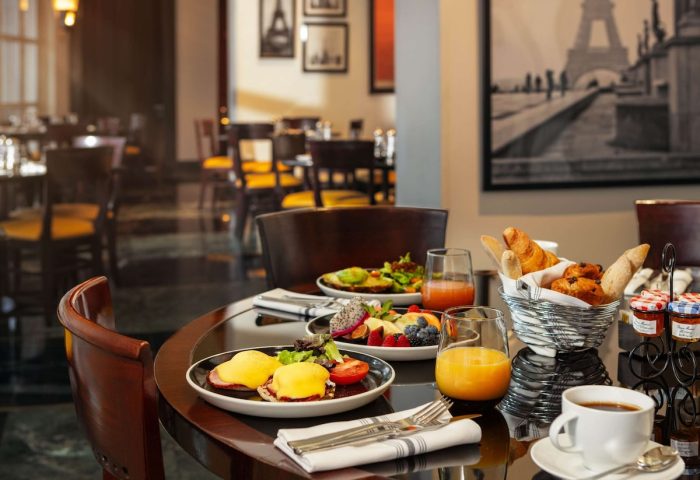 Sofitel New York gay-friendly hotel restaurant breakfast. Eggs Benedict, fruit, pastries, juice, and coffee on a table with Eiffel Tower art.
