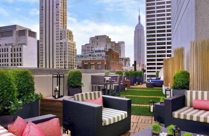 Sofitel New York gay-friendly hotel rooftop lounge. Empire State Building view, outdoor seating, plants, and city skyline.
