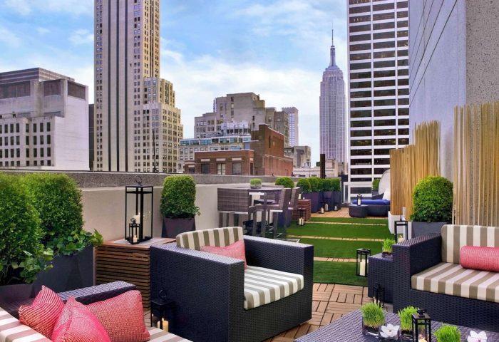 Sofitel New York gay-friendly hotel rooftop lounge. Empire State Building view, outdoor seating, plants, and city skyline.
