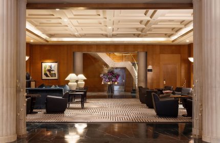 Sofitel New York's lobby. A gay-friendly hotel with stylish seating, a grand staircase, and elegant decor. Perfect for gay men's travel advice.