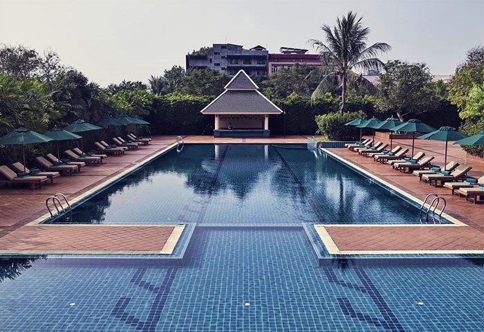 Sofitel Phnom Penh Phokeethra Hotel pool view. Gay-friendly hotel with sun loungers and umbrellas. Relaxing travel destination.