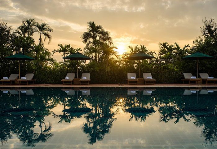 Poolside view at Sofitel Phnom Penh Phokeethra Hotel, a gay-friendly hotel. Lounge chairs & umbrellas reflect in the water at sunset.