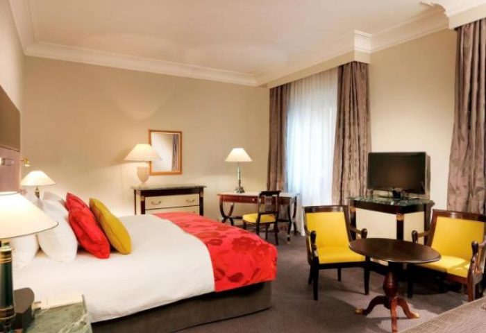 Gay-friendly Sofitel Rome Villa Borghese Hotel room. Bedroom with a bed, chairs, table, and TV. Luxury gay travel in Rome.