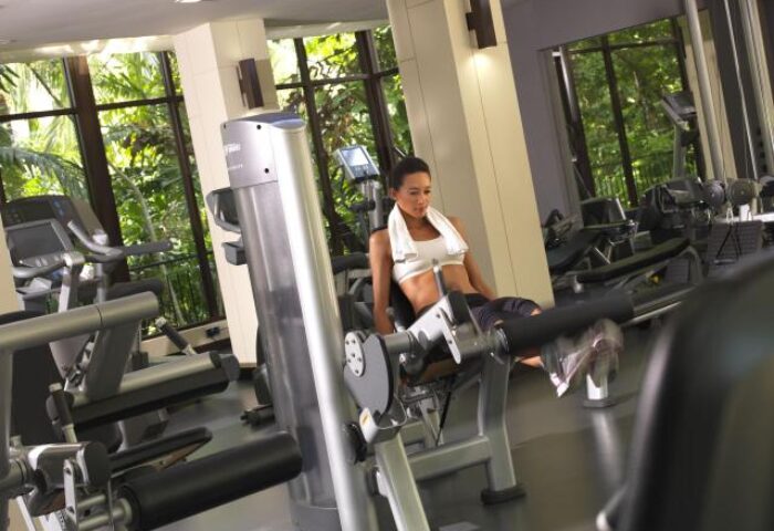 Gym at Sofitel Singapore Sentosa Resort & Spa, a gay-friendly hotel. Woman using leg extension machine. SG Clean Certified. Fitness while traveling.