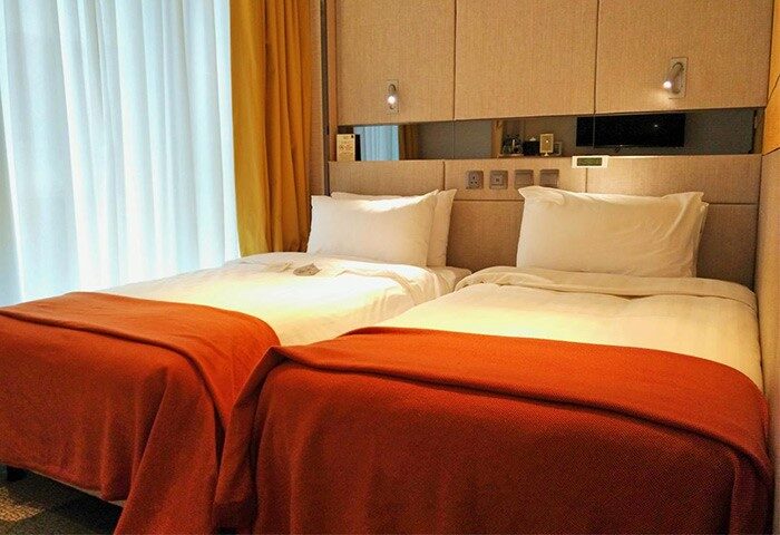 Sohotel's gay-friendly hotel room with two twin beds. Orange blankets add warmth. A comfortable space for gay travelers. Sohotel room interior.