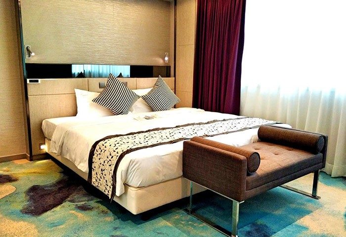 Sohotel gay-friendly hotel room: King bed with striped pillows, bench, and purple curtains. A comfortable stay for gay travelers.