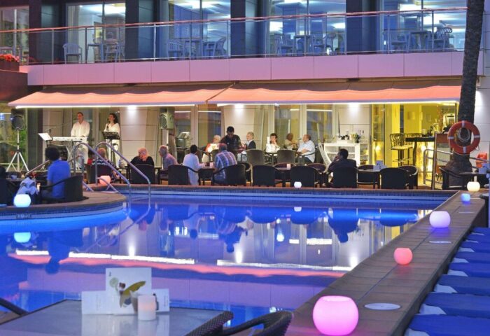 Sol Costablanca Adults-only hotel pool at night. People enjoy music, drinks. Gay-friendly hotel, perfect for gay men travel.