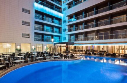 Sol Costablanca Adults-only hotel pool at night. Gay-friendly hotel with outdoor dining. Modern architecture and illuminated balconies.
