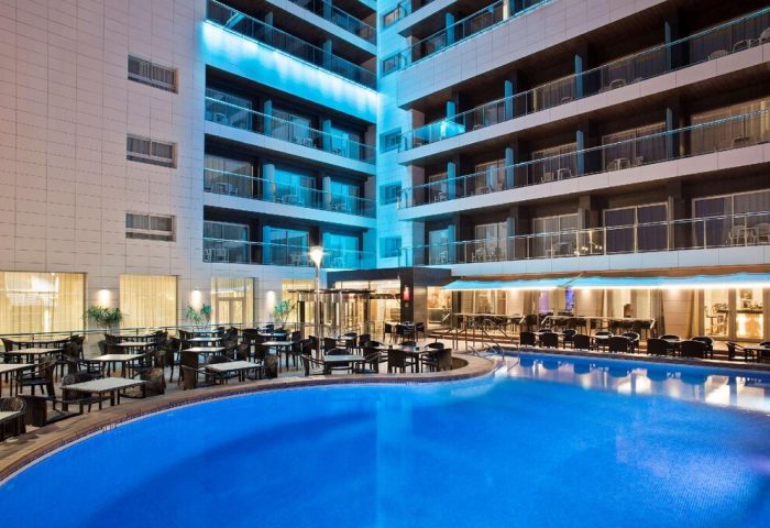 Sol Costablanca Adults-only hotel pool at night. Gay-friendly hotel with outdoor dining. Modern architecture and illuminated balconies.