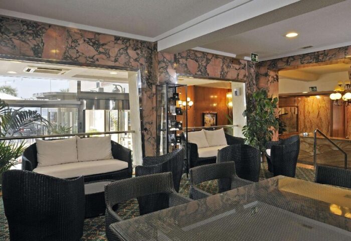 Sol Costablanca Adults-only hotel lobby. Seating area with rattan furniture, marble walls, and a view of the entrance. Gay-friendly hotel.
