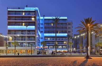 Sol Costablanca Adults-only hotel at night. Gay-friendly hotel with blue lights, balconies, palm trees, and beach view. Benidorm hotel.