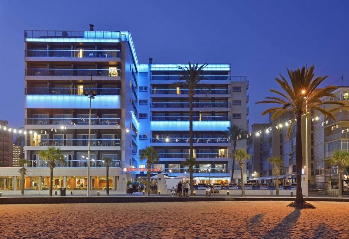 Sol Costablanca Adults-only hotel at night. Gay-friendly hotel with blue lights, balconies, palm trees, and beach view. Benidorm hotel.